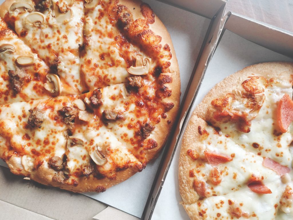 two round pizzas in boxes, one hawaiian and tomato, and one mushroom sausage