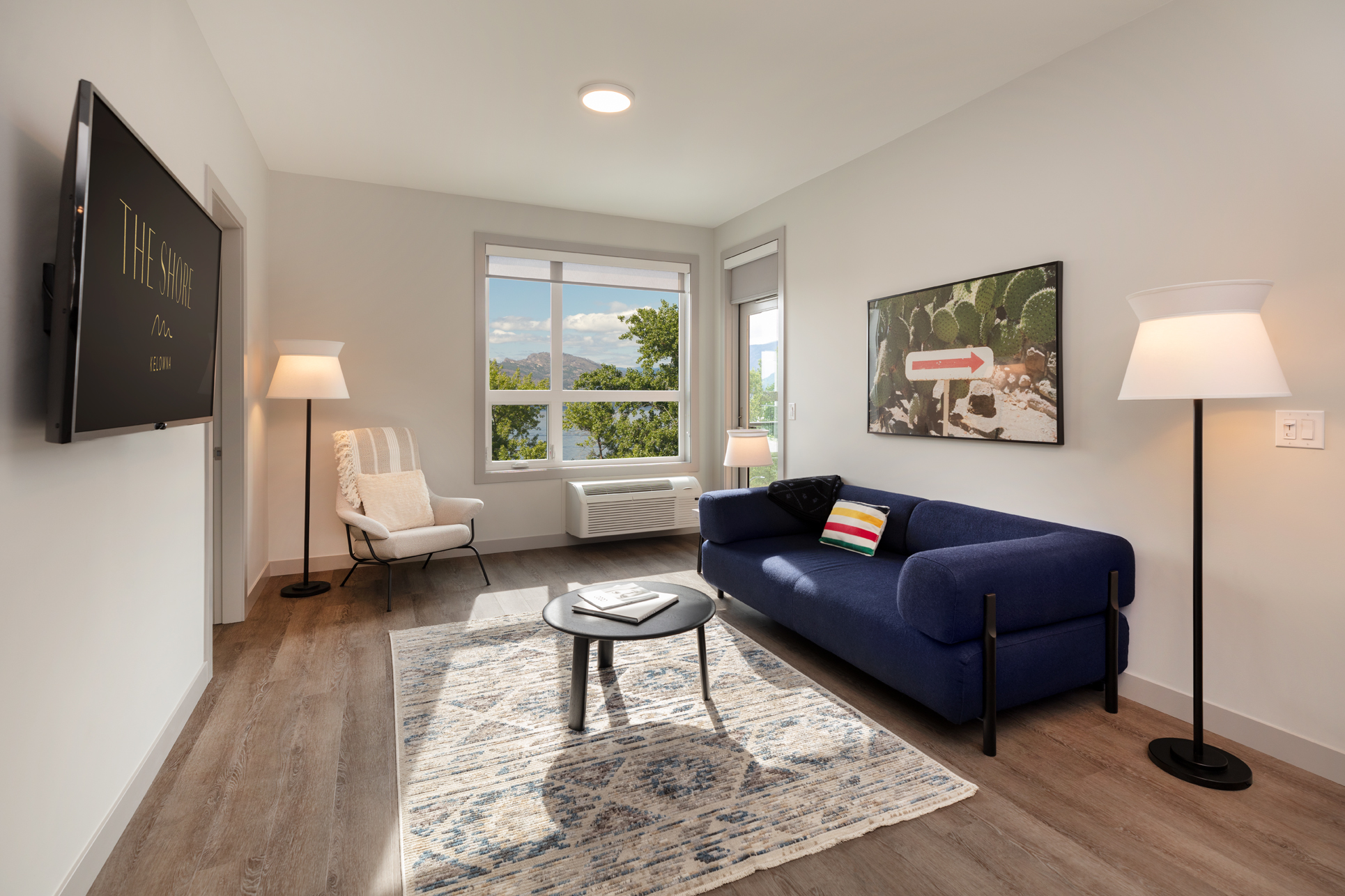 the living room in the 2 bedroom den suite at The Shore Kelowna, with a flatscreen TV, blue couch and decor items
