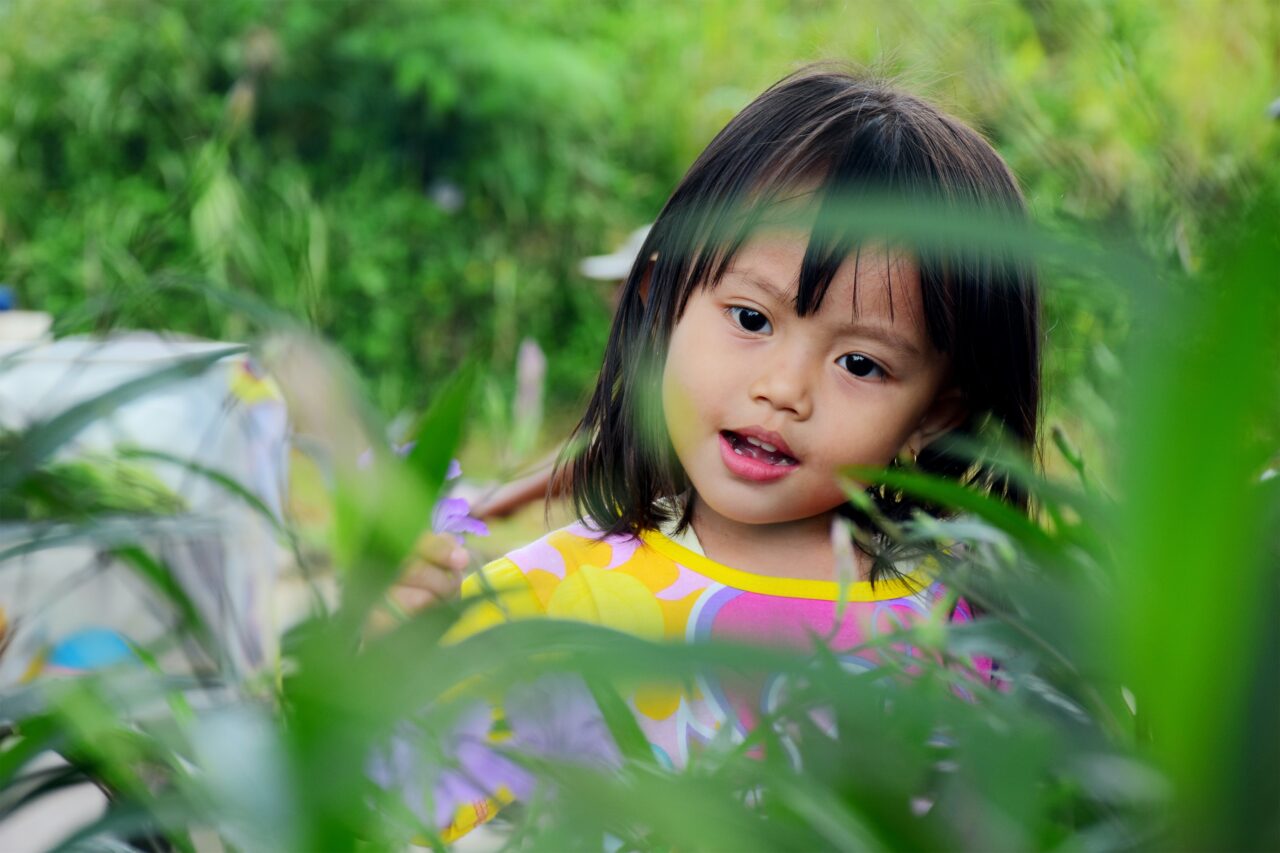 a young child at a park with grass in the foreground after having her hair cut with bangs