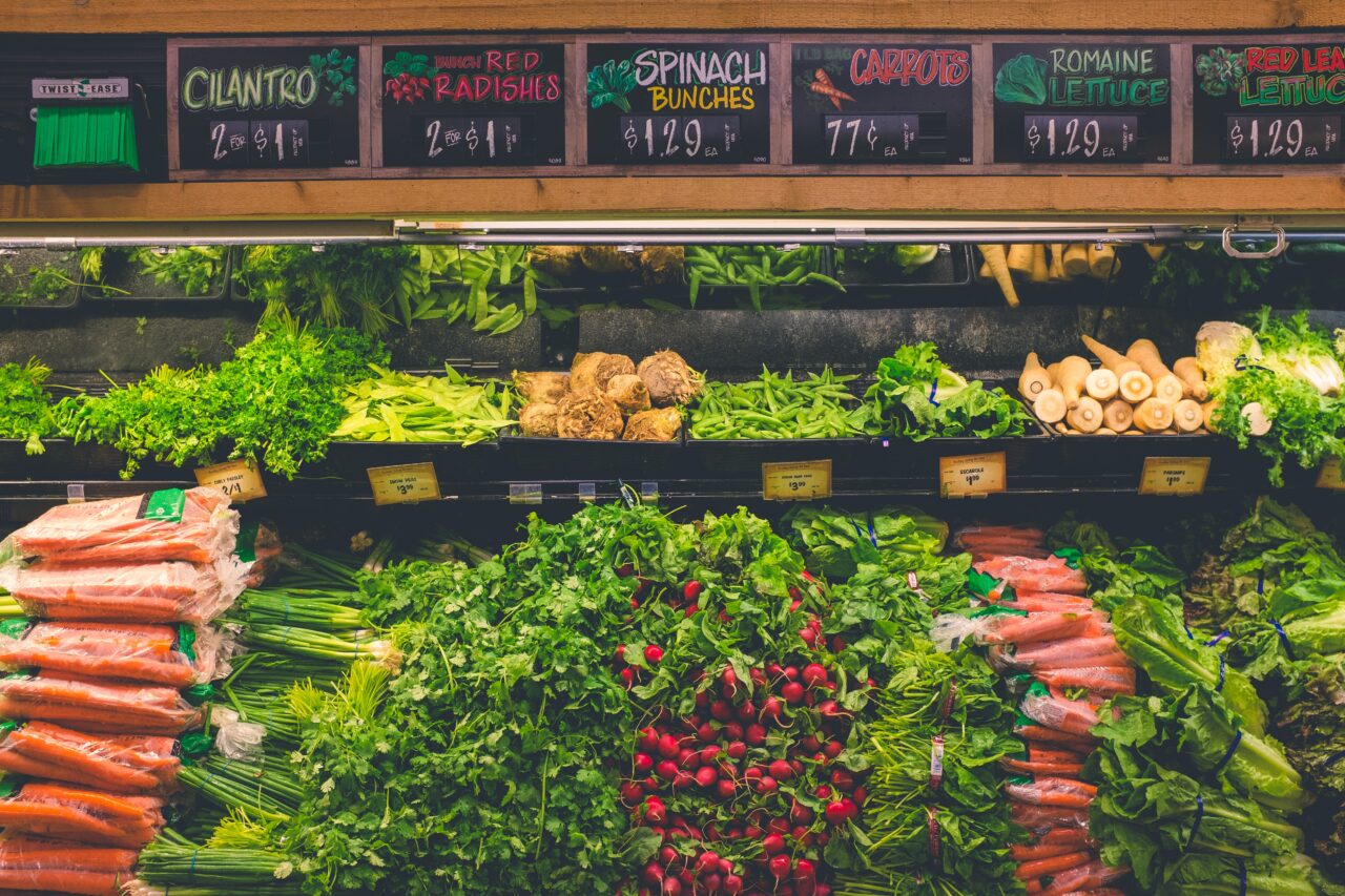 veggie section at the grocery store including carrots, leeks, radishes, lettuces, herbs, peas, and more