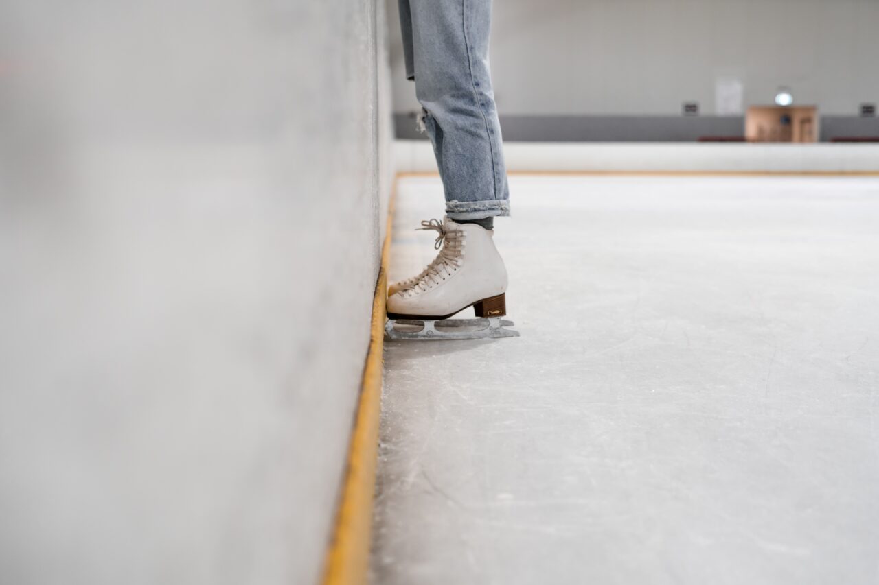 closeup of a woman wearing ice skates standing against the wall of an ice skating rink