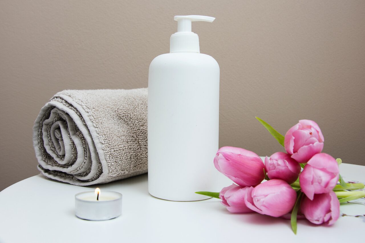a spa setup with a rolled up table, a lotion bottle, a tealight candle and tulips resting on a white table
