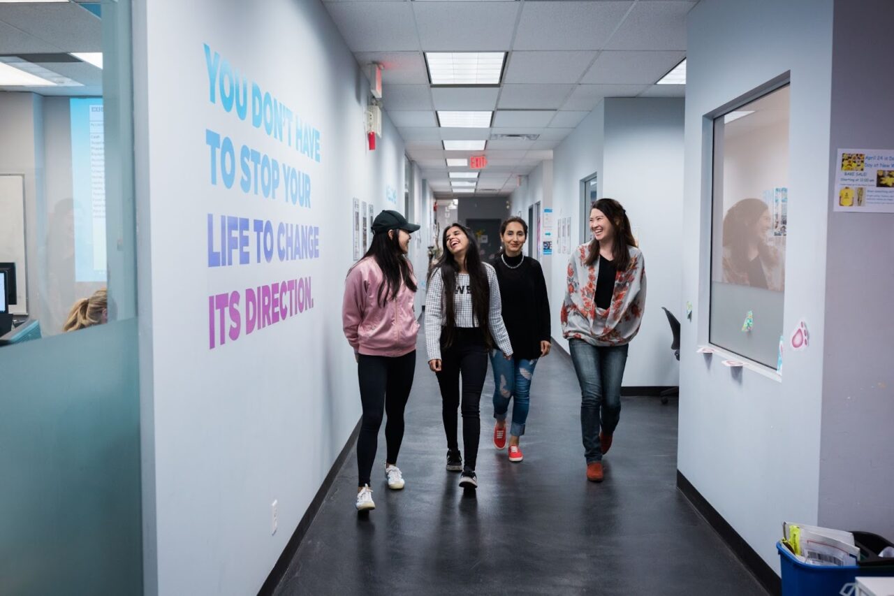 four young women walking down a corridor in the sprott shaw college kelowna campus, laughing and smiling