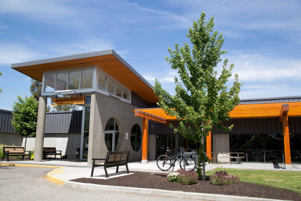 an exterior view of the Johnson Bentley Memorial Aquatic Centre, with benches and a bike racks in front of the entrance