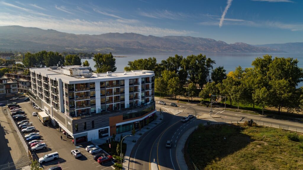 an exterior view of The Shore Kelowna, showing Gyro beach in front of the building and Okanagan Lake in the background