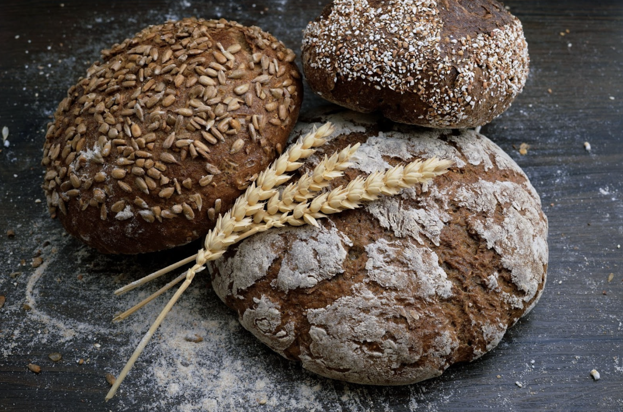 three loaves of bread sitting on a concrete counter with wheat on top at kelownas best bakeries