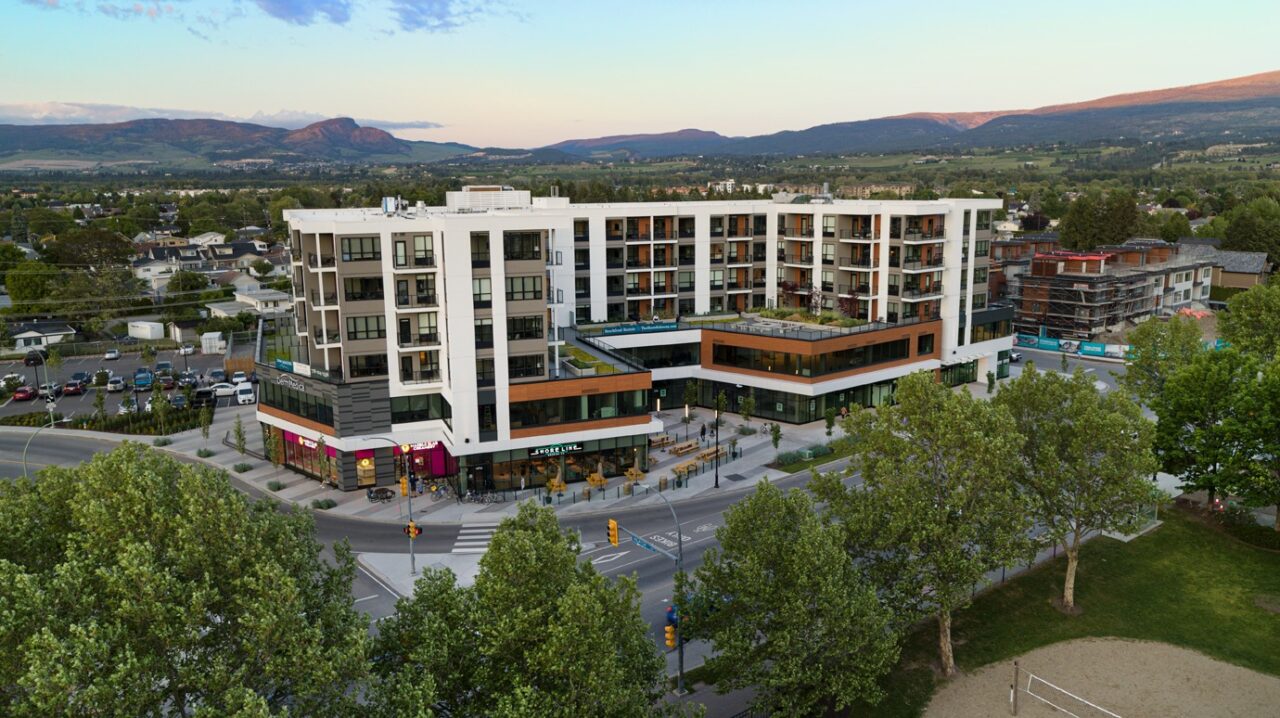 An exterior view of The Shore Kelowna, showing Gyro beach in the foreground and Shoreline Brewing on the ground level of the building