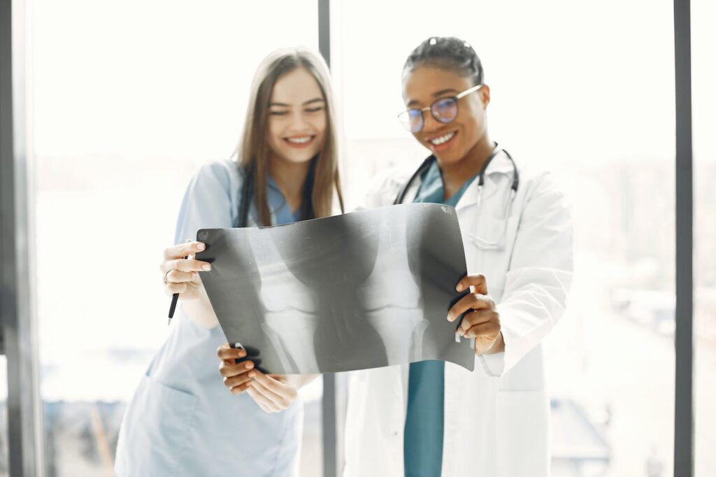 two kelowna health practitioners looking at an extra of a patients knees, with a bright window behind them