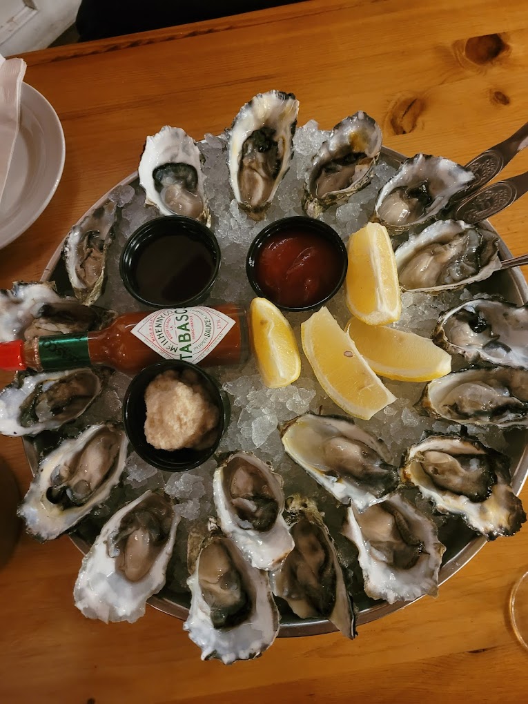 top-down view of oysters displayed on a bed of ice with lemon wedges and a bottle of hot sauce in the centre