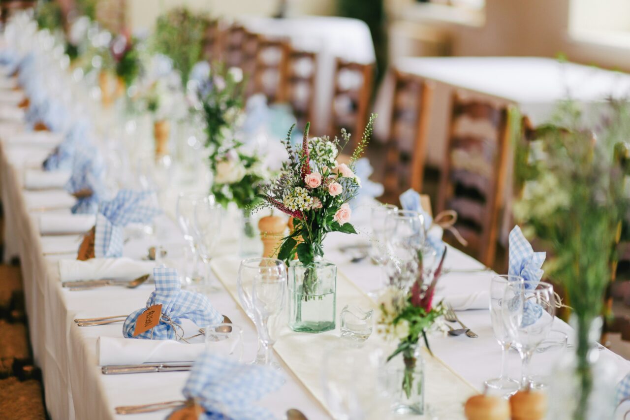 a wedding table with centrepieces of wild flowers and blue linen checkered bungled gifts for guests, with a white table cloth