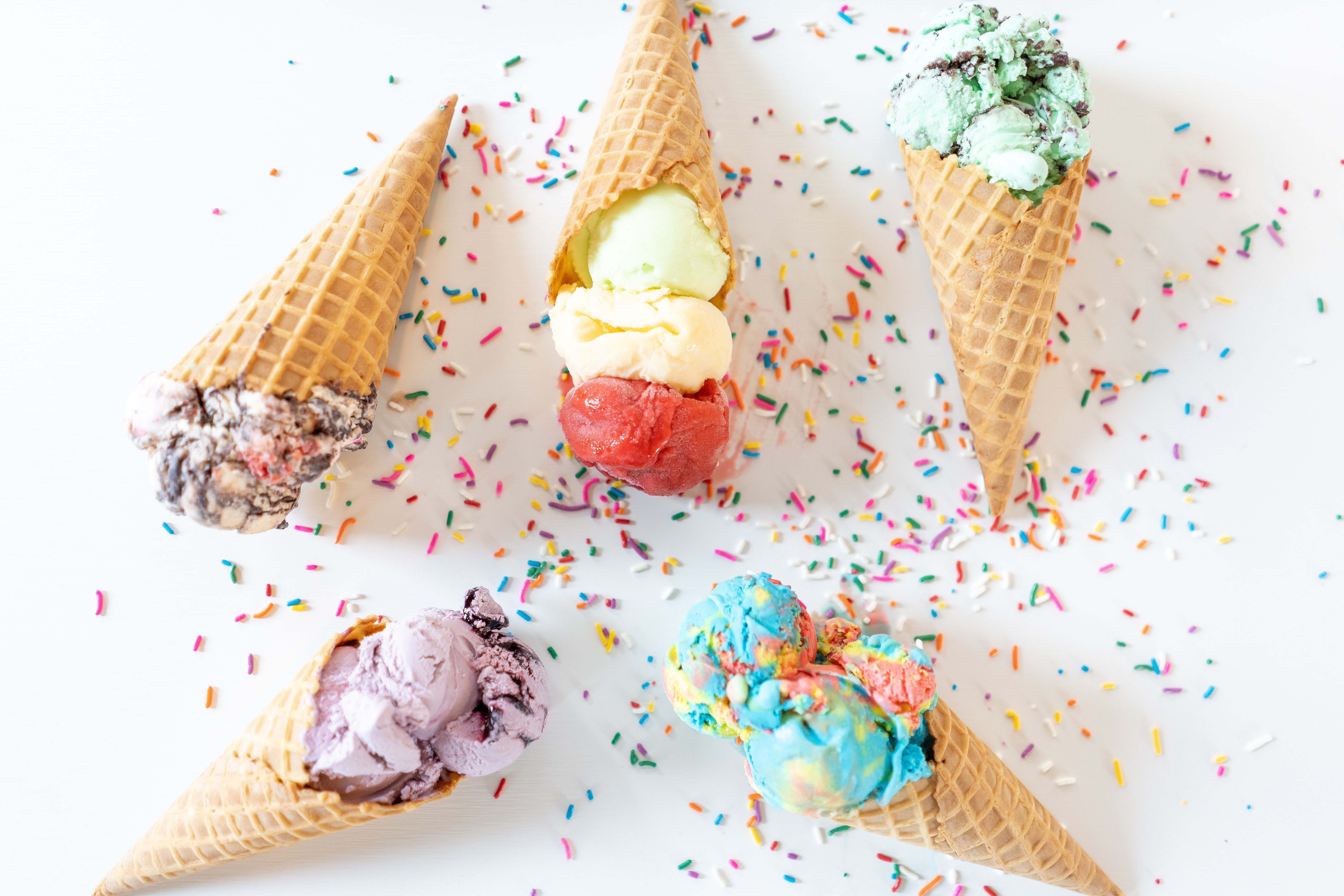 a white table with five ice cream waffle cones and scoops and sprinkles of varying colours, highlighting kelowna's best ice cream