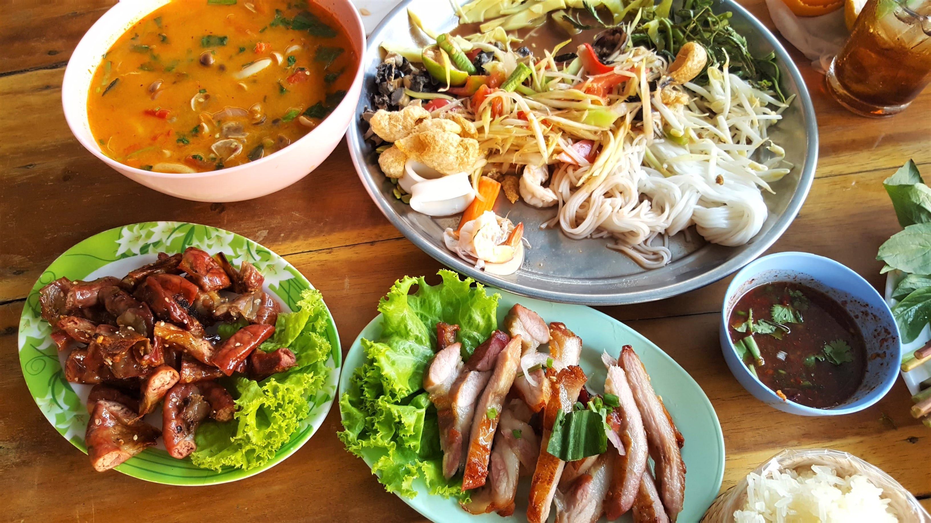 a spread of authentic kelowna thai food including curry, chicken and other dishes spread out on a table
