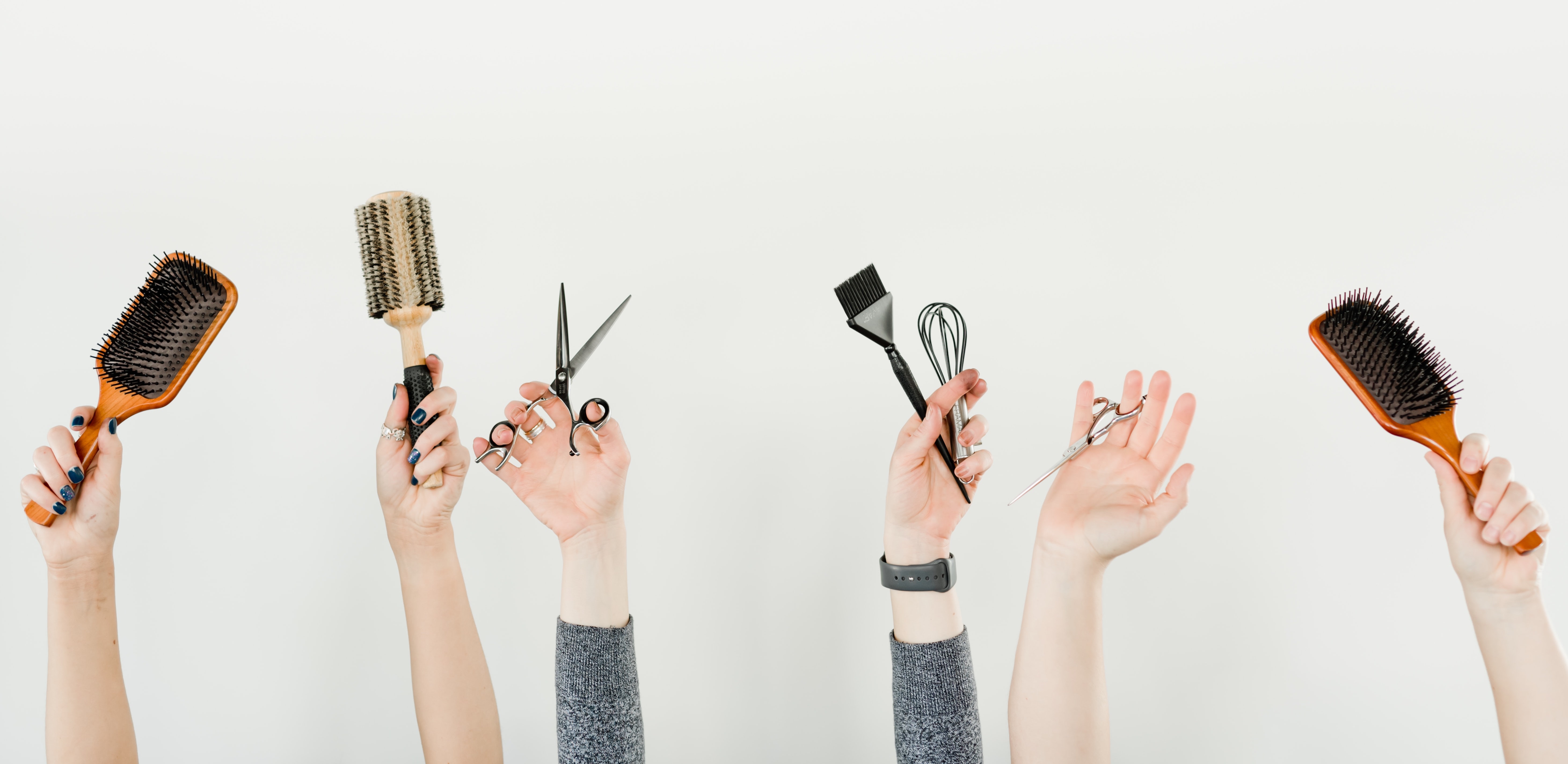 hands in the air holding hair scissors, brushes and combs to represent kelowna hair salons