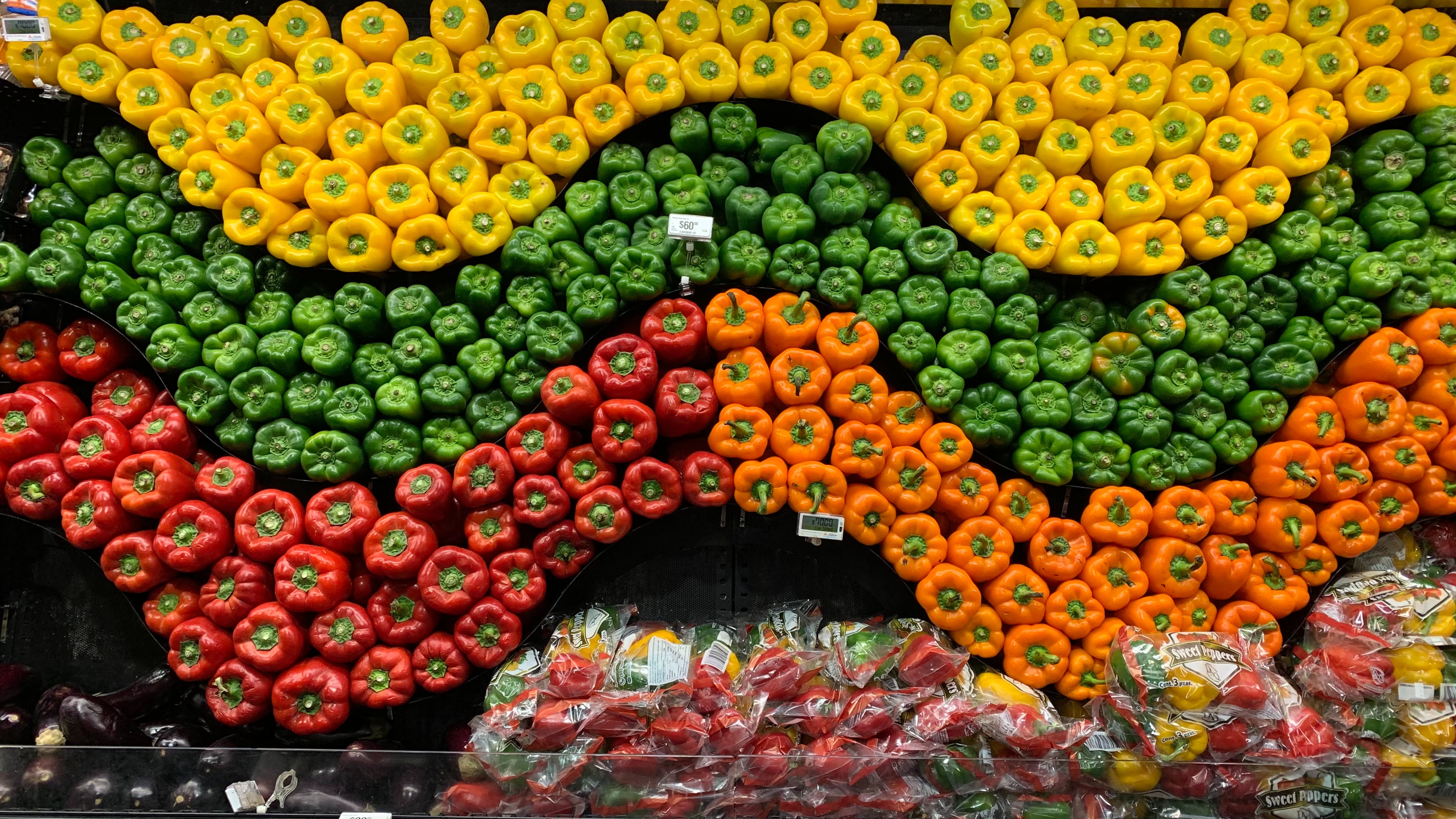 a wave pattern formed by yellow, green, red and orange bell peppers in a grocery store
