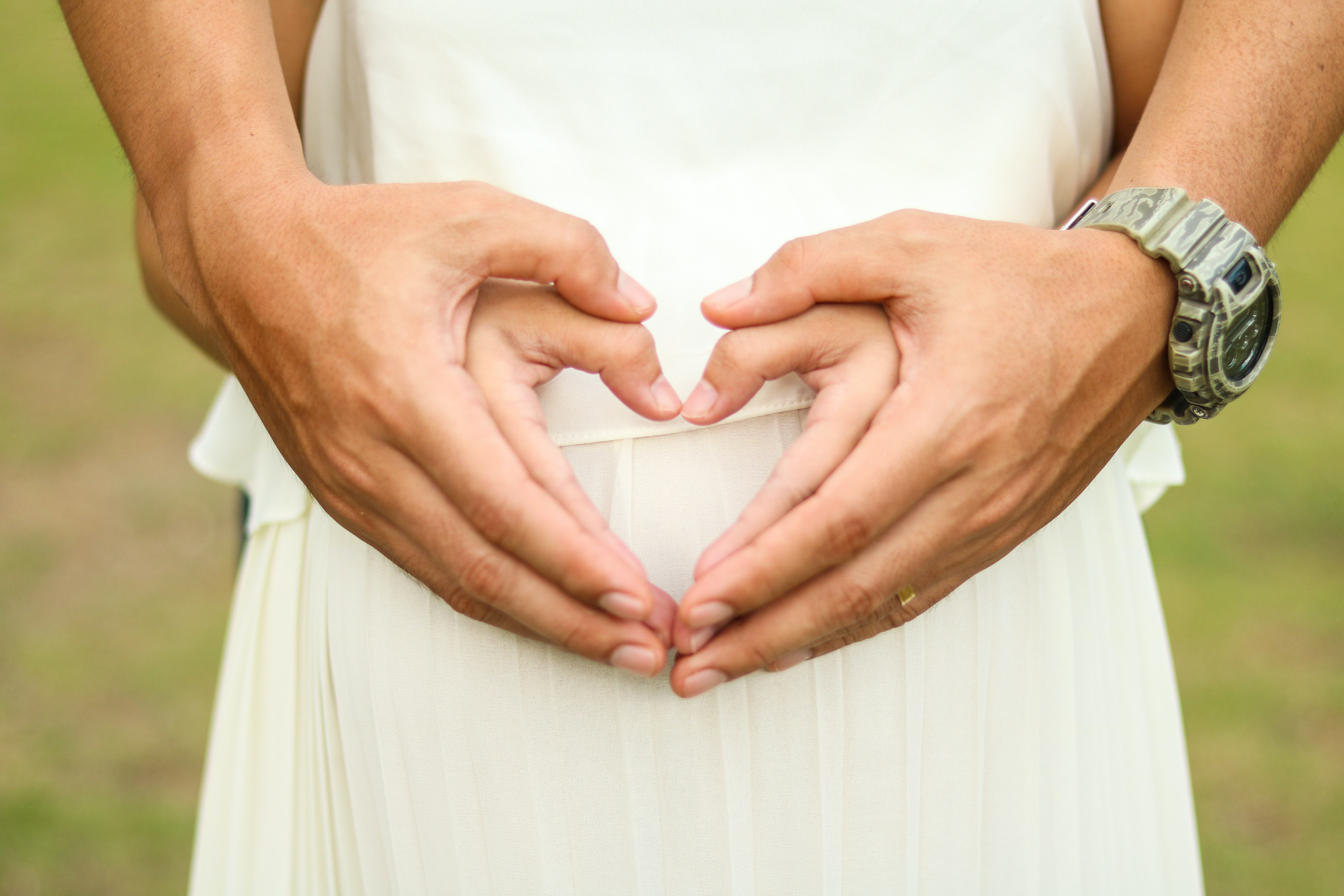 two sets of hands forming a heart shape over a pregnant womans belly, highlighting a kelowna babymoon