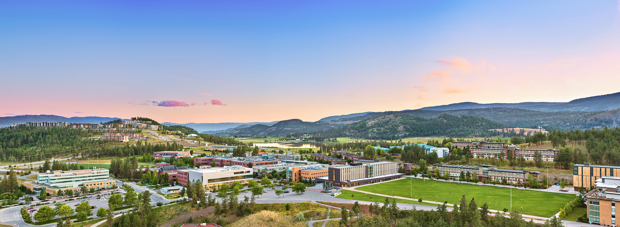 a view of the okanagan valley with UBCO kelowna university in the centre, surrounded by greenery, mountains and the lake in the background