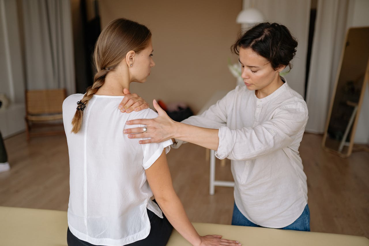 a kelowna health practitioner examining the shoulder of a patient sitting on a massage table in a clinic setting