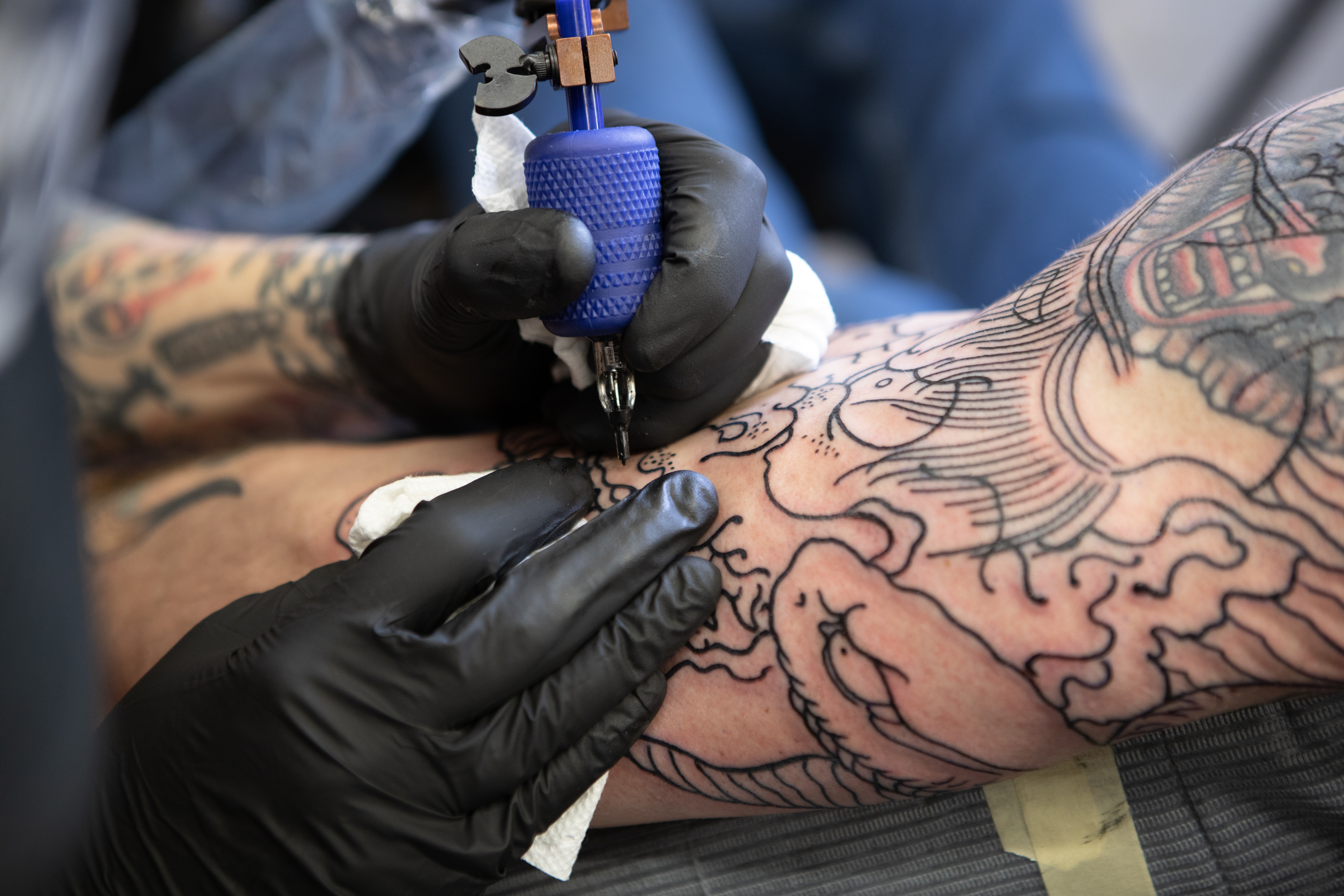 a kelowna tattoo artist closeup of their hands tattooing an arm with outline traditional style