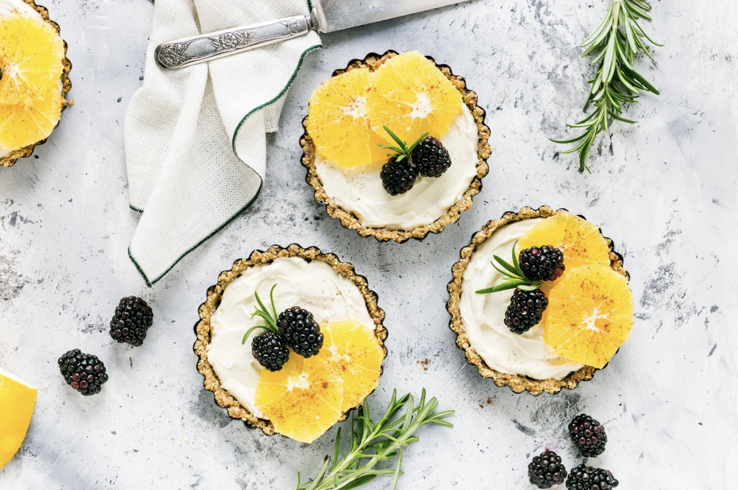 a top-down view of mandarin blackberry tarts on a marble countertop with rosemary sprigs as garnish, highlighting the best desserts in kelowna