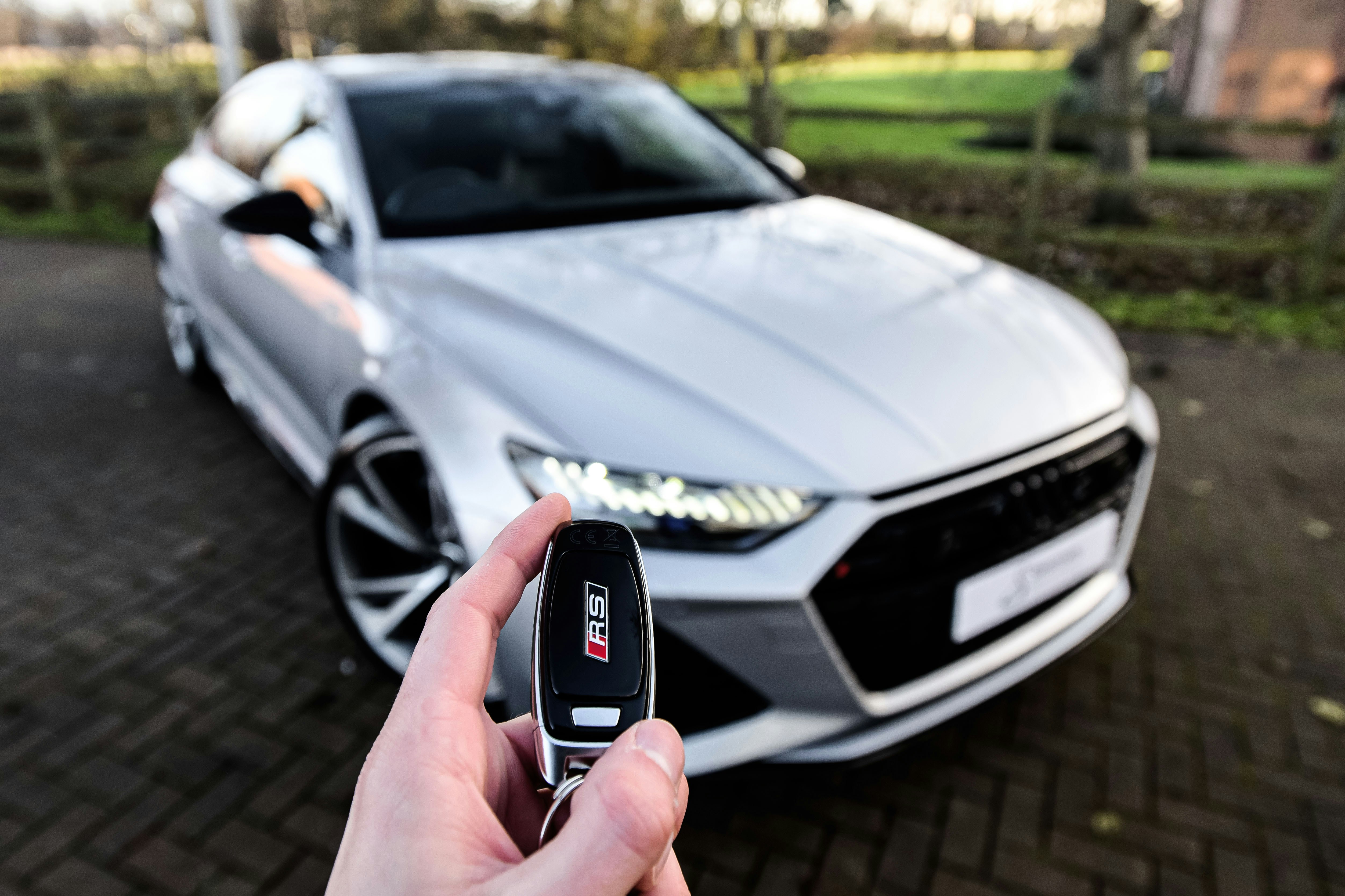 A hand holding an electronic car key in front of a silver car, highlighting car shopping in Kelowna