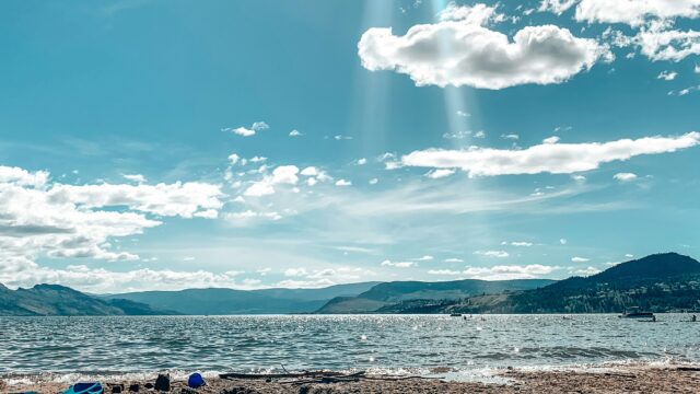 A view of Okanagan Lake from the beach under a beautiful blue sky with a few white clouds.